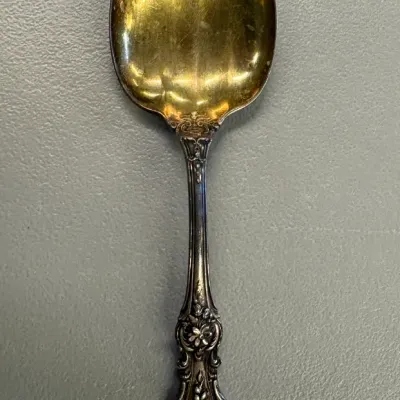 Ornate sterling silver spoon with a gold-washed bowl and a highly detailed floral handle, showing some tarnish and wear.
