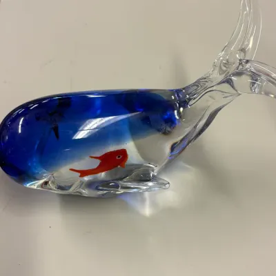 Murano-style art glass whale paperweight, featuring a clear and blue body with an encased red fish figurine.