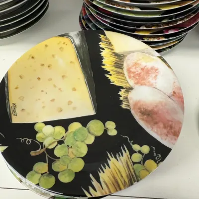 Stack of contemporary ceramic plates featuring a black background with colorful illustrations of cheese, bread, and grapes.