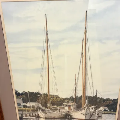 Framed and matted nautical art print depicting two masted sailboats docked in a harbor, signed and numbered in the lower right corner.