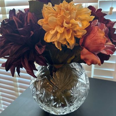 Sale Photo Thumbnail #537: Round cut crystal or heavy glass rose bowl vase featuring a starburst and criss-cross cut pattern, filled with an arrangement of faux flowers including autumn-toned roses and dahlias in shades of burgundy, orange, yellow, and purple. Vase and artificial f