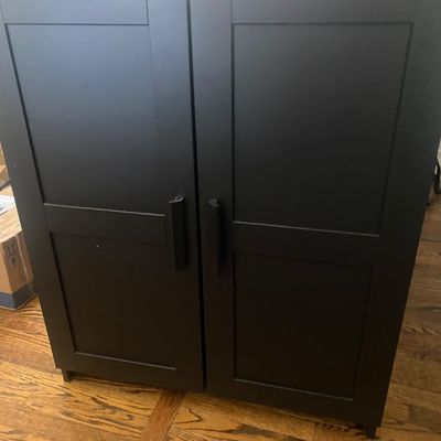 Sale Photo Thumbnail #531: Modern black double-door accent storage cabinet featuring shaker-style door panels and matching vertical handles. Open interior space without interior shelves currently installed (shelf pin holes present for adjustability). Minor superficial edge wear on 