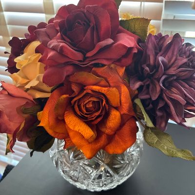 Sale Photo Thumbnail #538: Round cut crystal or heavy glass rose bowl vase featuring a starburst and criss-cross cut pattern, filled with an arrangement of faux flowers including autumn-toned roses and dahlias in shades of burgundy, orange, yellow, and purple. Vase and artificial f