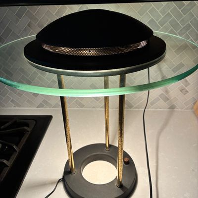 Sale Photo Thumbnail #553: Postmodern halogen desk lamp featuring a round black base, three brass-tone columnar supports, a clear thick glass disc diffuser collar, and a black dome top with perforated ventilation mesh. Powers on and lights up as shown. Shows light age-appropriate p