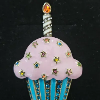 Sale Photo Thumbnail #188: Heidi Daus "Captivating Cupcake" Brooch featuring pink enamel frosting, multi-colored star crystals, a striped candle with an orange flame, and a bright blue crystal-paved wrapper