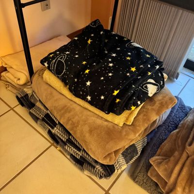 Stack of assorted throw blankets, including a black fleece blanket with a yellow star and planet pattern, a solid tan plush blanket, and...