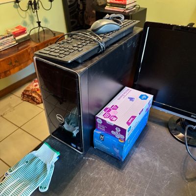 Dell desktop computer tower with a wired keyboard and mouse resting on top, shown alongside a monitor and boxes of nitrile gloves.