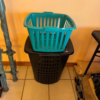 Teal plastic laundry basket stacked on top of a black plastic laundry hamper with a lid.