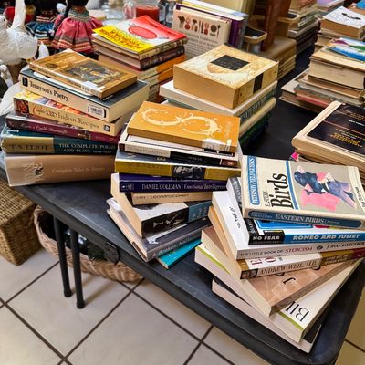 A large collection of vintage and modern books, including poetry, field guides, and literature, stacked on a black folding table.