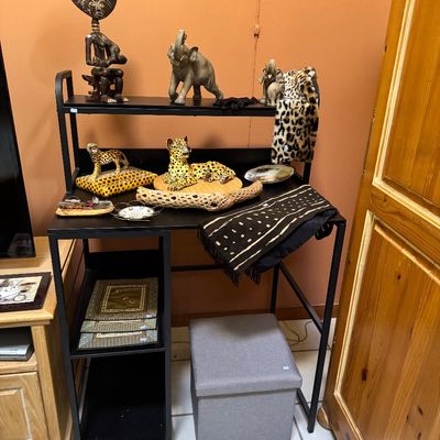 Black metal frame desk with built-in shelving, displaying various African-themed decor items including leopard figurines, elephant...