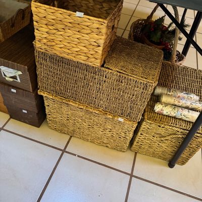 Assorted woven storage baskets in various sizes and styles, stacked alongside brown cardboard storage boxes.