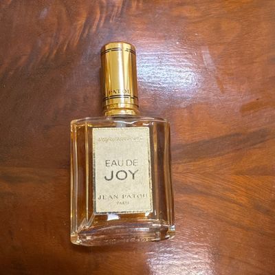 Vintage bottle of Eau de Joy by Jean Patou Paris, featuring a gold-tone cap and partially filled glass bottle.