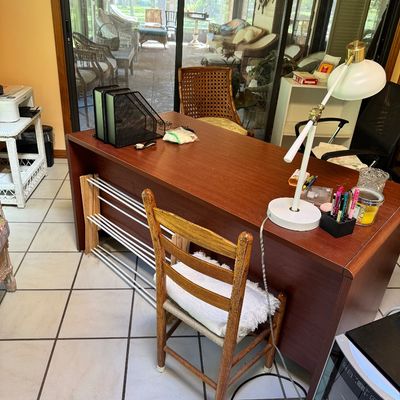 Mid-century modern style wooden desk with a ladder-back chair, featuring a white adjustable desk lamp and various office accessories.
