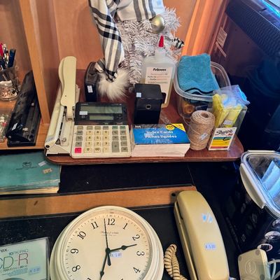 Assorted desk and office supplies, including a Casio calculator, a vintage-style wall clock, a beige landline telephone, and various...