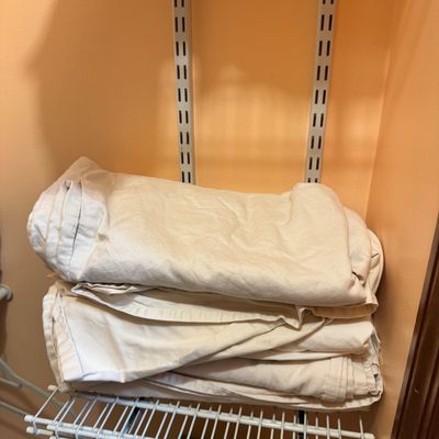 Stack of folded white canvas drop cloths or heavy utility fabric resting on a wire closet shelf.