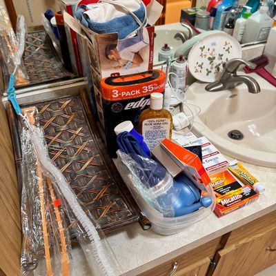 Assorted bathroom and personal care items, including a woven tray, drain cleaning tools, aloe vera gel, shaving cream, and first aid...