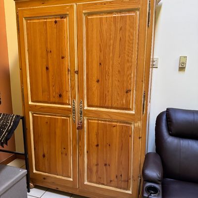 Rustic pine armoire featuring two large paneled doors with ornate brass hardware and a tassel detail.