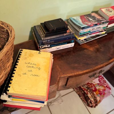 Assorted vintage books and cookbooks, including a spiral-bound "What's Cooking at St. Rose" community cookbook, displayed...