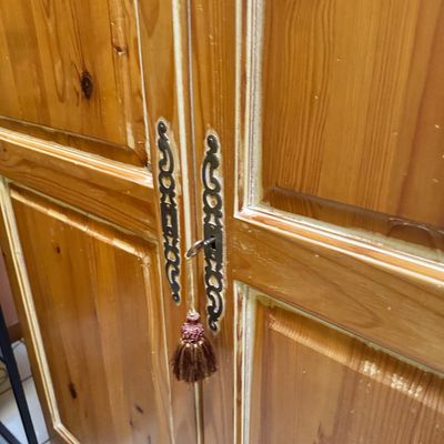 Vintage pine armoire featuring ornate brass keyhole escutcheons and a key adorned with a decorative brown tassel.