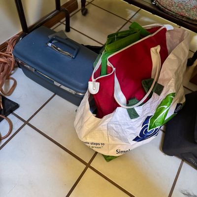 Vintage Samsonite blue hard-shell train case alongside reusable shopping bags filled with items on a tiled floor.