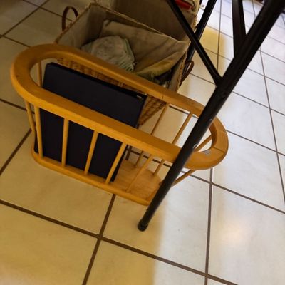 Vintage wooden spindle-sided magazine rack in a light finish, shown holding a dark blue binder, alongside woven storage baskets on a...