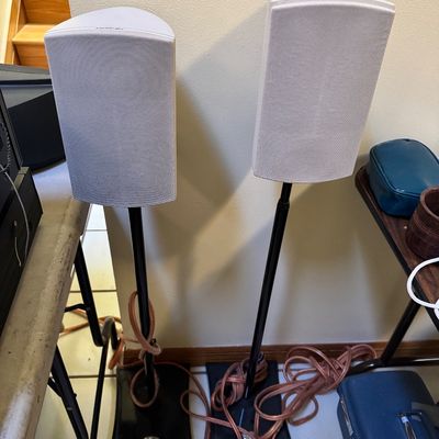 Pair of white Definitive Technology surround sound speakers mounted on black metal floor stands, complete with speaker wire.
