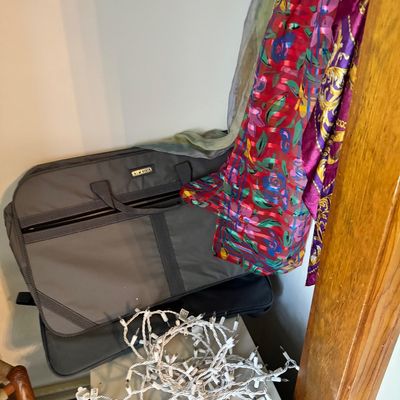 Assorted items including a grey soft-sided garment bag, a tangled strand of white Christmas lights, and several colorful patterned...