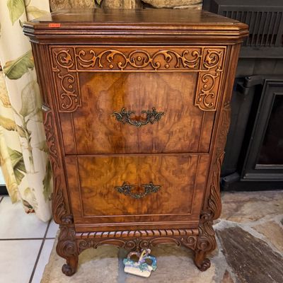 Vintage ornate two-drawer wooden nightstand or chest featuring burl wood veneer, elaborate scrollwork carvings, and decorative brass pulls.
