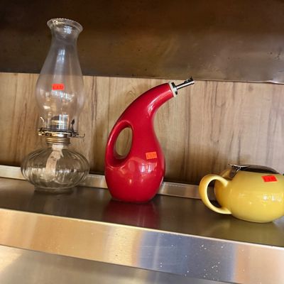 Assorted kitchenware including a vintage clear glass oil lamp, a modern red ceramic oil dispenser, and a yellow ceramic teapot with a...