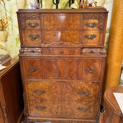 Vintage French Provincial style tallboy chest of drawers featuring ornate wood carvings, burl wood veneer drawer fronts, and decorative...