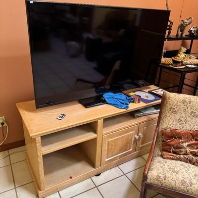 Large flat-screen television sitting on a light oak media console with open shelving and double doors.