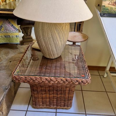 Woven wicker side table with a glass top, paired with a large ceramic table lamp featuring a textured leaf pattern and a wide fabric shade.