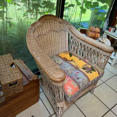 Vintage wicker armchair with a high back, wide armrests, and a colorful patchwork floral cushion.