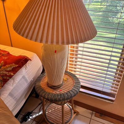 Vintage 1980s ceramic table lamp with a textured, wavy design and a pleated fabric shade, displayed on a two-tier wicker and rattan side...