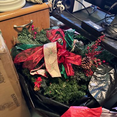Assorted Christmas greenery and decorations, including a faux pine wreath adorned with red and green ribbons, pinecones, and red berries.