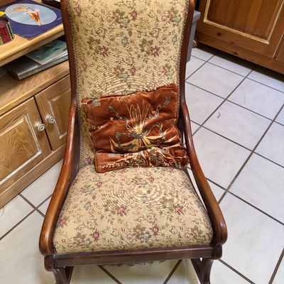 Vintage wooden rocking chair featuring floral tapestry upholstery and a coordinating rust-colored velvet accent pillow.