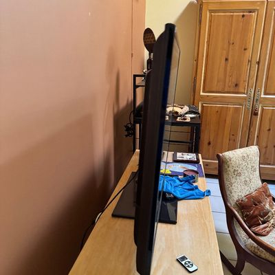 Side profile of a flat-screen television on a light wood console table, shown alongside a remote control.