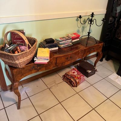 Vintage Italian provincial style console table with cabriole legs and drawers, holding books, a wicker basket of media, and a black metal...