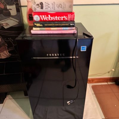 Frestec black compact mini fridge with an Energy Star rating, shown with a stack of books on top.