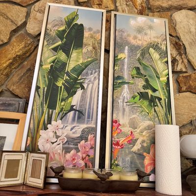 Pair of vintage tropical waterfall landscape prints in silver-toned frames, featuring lush banana leaves, orchids, and hibiscus flowers.