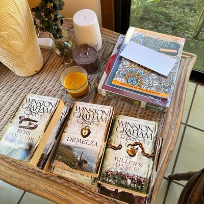 Selection of Winston Graham paperback books, including Ross Poldark, Demelza, and The Miller's Dance, displayed alongside coloring...