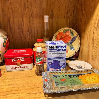 Assorted household items on a wooden shelf, including a vintage Campbell's Soup recipe tin, a NeilMed Neti Pot box, decorative...