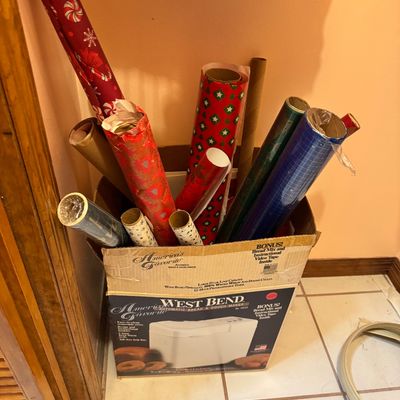 Assorted rolls of holiday and decorative wrapping paper stored in a vintage West Bend bread maker cardboard box.