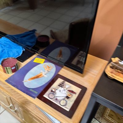 Vintage framed art pieces, including a ballerina illustration and a whimsical chef on a bicycle print, displayed on a light wood media...