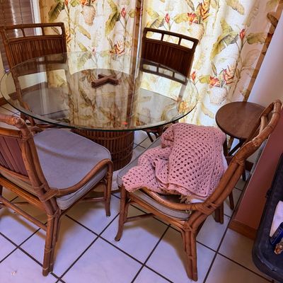 Vintage rattan dining set featuring a round glass-top table with a woven pedestal base and four matching high-back chairs with...