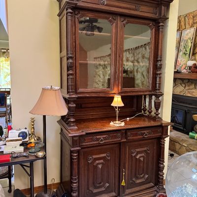 Antique carved oak hutch featuring a glass-front upper cabinet, turned columns, and a lower buffet with two drawers and two paneled doors.