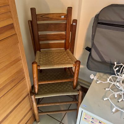 Pair of vintage ladderback chairs with woven rush seats, stacked in a corner.