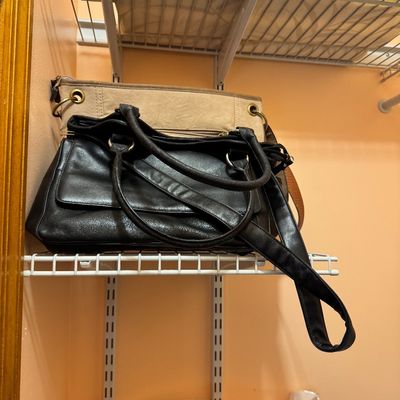 Two women's handbags, including a black faux leather shoulder bag and a beige canvas tote, displayed on a wire closet shelf.