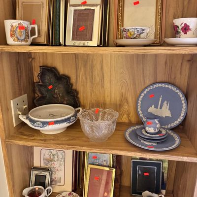 Wooden bookshelf displaying various vintage collectibles, including picture frames, teacups, a blue and white tureen, a clear glass bowl,...