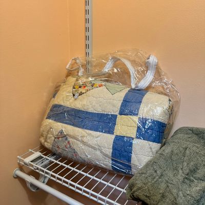 Vintage handmade patchwork quilt with blue and white blocks, stored in a clear zippered plastic bag on a wire closet shelf.
